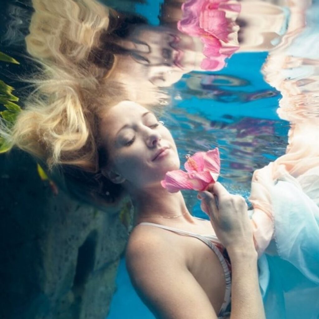 Woman floating underwater with pink flowers during a hydration facial ritual at Lahaina Luxury Health Spa Maui. Photograph by Kelly Hsiao