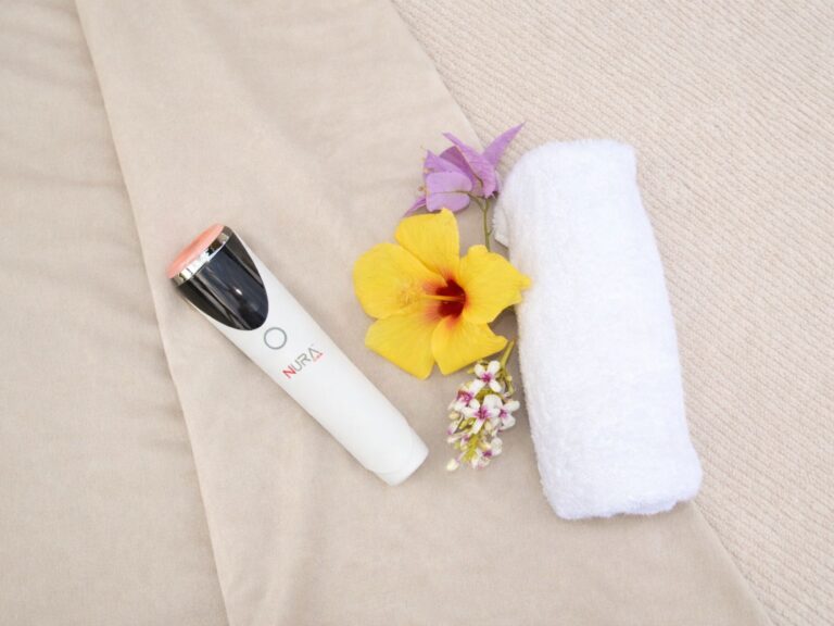 NURA red light therapy device on beige linens with hibiscus flowers and spa towel